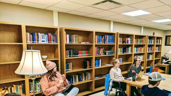 Students gathered seated in a small space with bookshelves lining walls